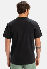Czarny T-shirt z krótkim rękawem, z okrągłym dekoltem, wykonany z miękkiej bawełny. Tył ma gładką teksturę i luźny krój.