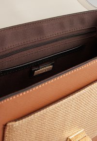 Gros plan de l'intérieur d'un sac à main beige et marron texturé avec une doublure en tissu marron et une poche zippée noire.
