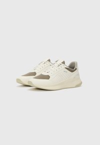 Weiße Sneakers mit hellbraunen Mesh-Akzenten, durchbrochener Detailarbeit und einer strukturierten Sohle. Verfügt über Schnürsenkel und Branding auf der Seitenfläche.