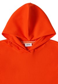 Sweat à capuche en tissu côtelé orange vif avec une grande capuche et une étiquette blanche affichant le nom de la marque "CECIL" à l'intérieur de l'encolure.