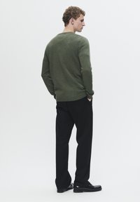 Olivgrüner Stricksweater mit langen Ärmeln und rundem Kragen, kombiniert mit schwarzen Hosen und glänzenden Schuhen, von hinten betrachtet.