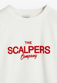 Sudadera blanca con texto bordado en rojo "THE SCALPERS Company." Presenta un escote redondo y mangas raglán. Textura de tela suave.