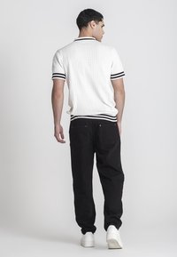 Polo blanco de punto con un patrón texturizado, rayas negras en el cuello y los puños, combinado con pantalones negros y zapatillas blancas.