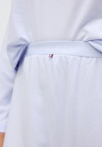 Svetlo modro bombažno oblačilo z elastiko v pasu, na kateri je napis "TOMMY HILFIGER", ter majhen trifarben poudarek blizu šiva.