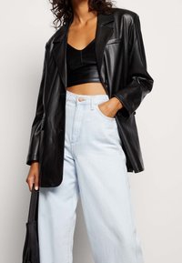 Černý kožený oversize blazer s klopami, spárovaný s černým crop topem a světle modrými džíny s vysokým pasem. Texturovaný povrch.