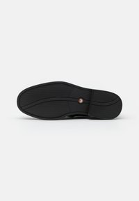 Semelle d'une chaussure habillée noire avec une semelle texturée et des détails de lignes courbes, présentée sur un fond blanc uni.