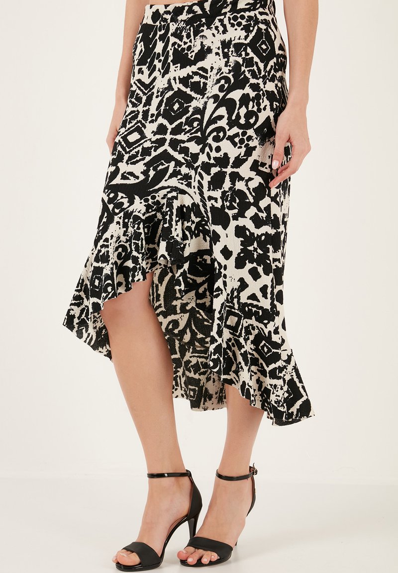 Jupe midi à motif noir et blanc avec un ourlet froncé, présentant une fente haute et une taille élastique, associée à des talons aiguilles noirs à lanières.