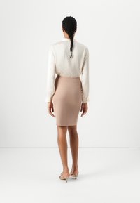 Šviesiai smėlinis marškinėliai su subtilia tekstūra, derinami su prigludusia nude spalvos pieštuko sijonu. Modelis nešioja permatomas kulkšnines sandalus. Atgalinis vaizdas.