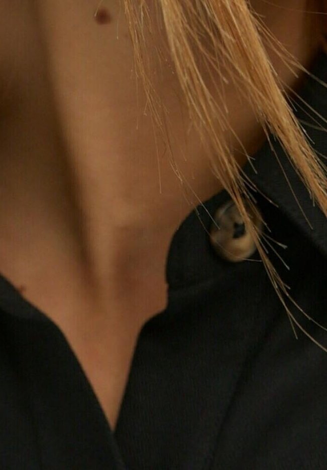 Gros plan d'un décolleté avec des mèches de cheveux clairs sur la peau et un col de chemise noir avec un bouton visible.