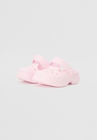 Vaaleanpunaiset puukengät, jotka on valmistettu kevyestä materiaalista, jossa on ilmanvaihtorei'ät, takahihna ja paksu, uritettu pohja.