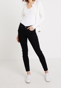 Czarne, wąskie dżinsy wykonane z denimu, w parze z białym topem na ramiączkach i jasnym kardiganem. Białe sneakersy dopełniają zestaw. Prosty, dopasowany krój.