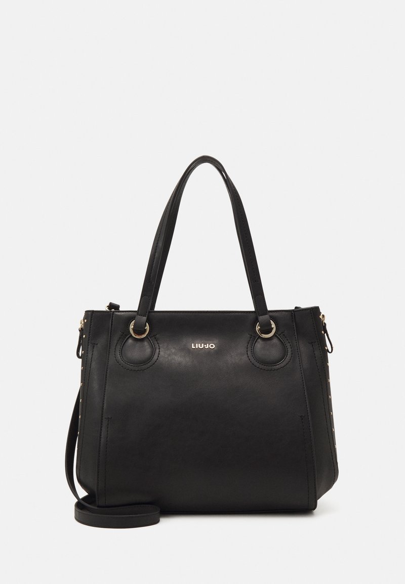 Bolsa tote de piel sintética negra con asas dobles, detalle del logotipo y acentos en hardware en tono dorado. Presenta una forma estructurada y un diseño lateral con tachuelas.