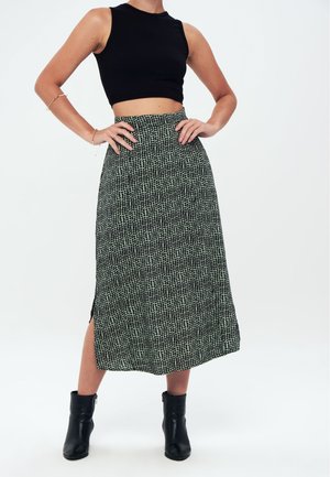 Zwarte geribde crop top gecombineerd met een lange, gestructureerde rok met een groen en zwart patroon en een split aan de zijkant, afgemaakt met zwarte enkellaarsjes.