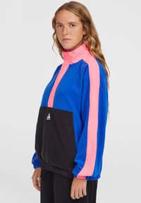 Farverig pullover med høj krave. Har blå krop, rosa skulderstriber og en sort frontlomme. Blød tekstur og elastiske manchetter.