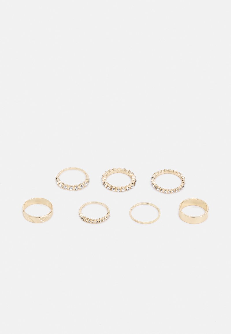 Ensemble de sept bagues en or avec des designs variés, y compris des bands lisses, des accents cloutés et des surfaces texturées. Certaines présentent des pierres transparentes.