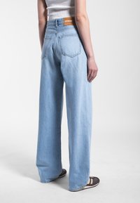 Lichtblauwe wijd been jeans van denim met een hoge taille, zichtbare achterzakken en een bruine merklabel genaaid in de tailleband.