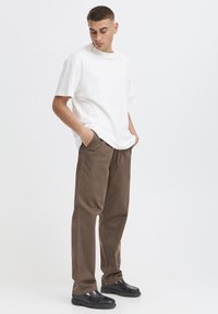 T-shirt in cotone bianco dal taglio morbido, abbinata a pantaloni marroni a gamba stretta e scarpe nere con plateau, che mostrano un design casual.