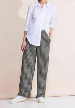 Camisa blanca abotonada con mangas remangadas, combinada con pantalones anchos de pierna ancha con estampado en blanco y negro y zapatillas blancas. Estilo y ajuste sencillos.