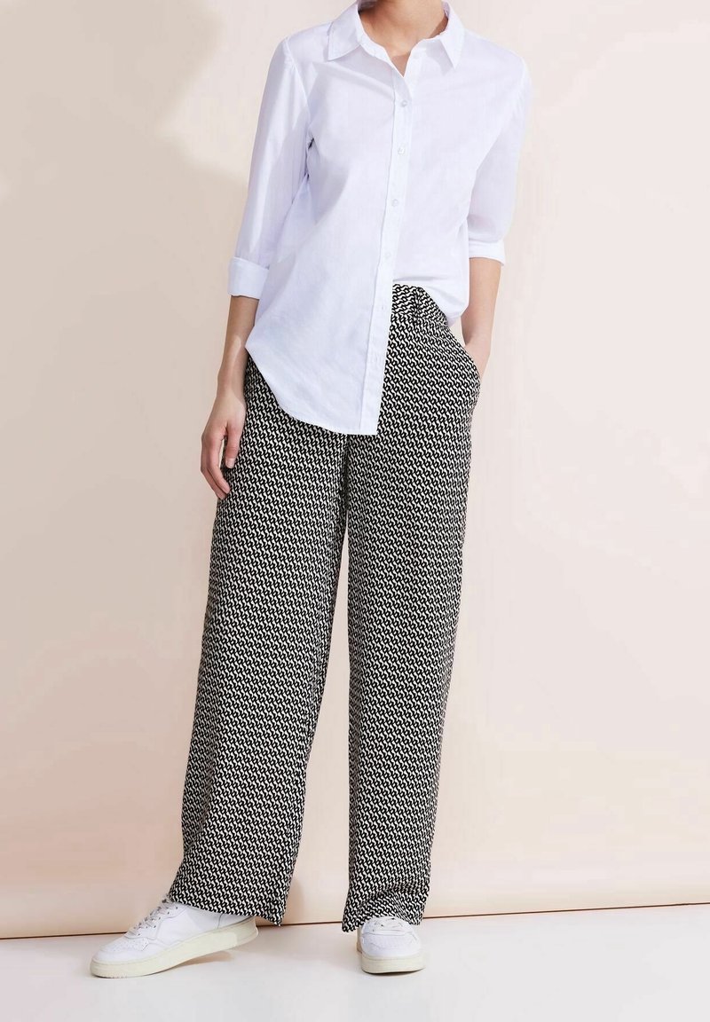 Chemise blanche à boutons avec manches retroussées, associée à un pantalon large à motifs noirs et blancs et des baskets blanches. Style simple et coupe confortable.