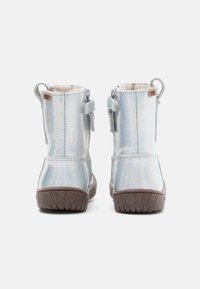 Sølv ankelstøvler med en teksturert, iridescent finish. Fuzzy fôr synlig på toppen, sikret med justerbare stropper. Gummisåle.
