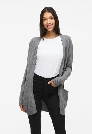 Gray knit cardigan with open front, ribbed cuffs, and two front pockets, paired with a white shirt and black pants. Smooth texture.