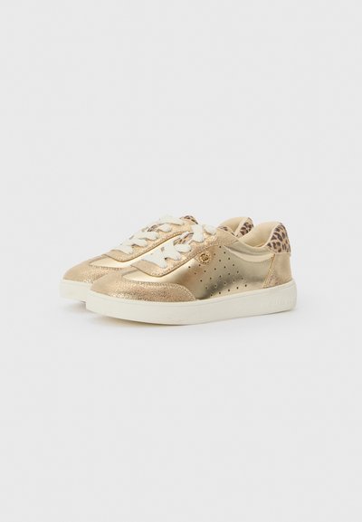 Zapatillas metálicas doradas con acentos perforados, cordones beige, cuello acolchado en el tobillo y un detalle de estampado de leopardo en el talón sobre una suela blanca.