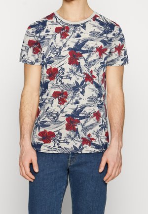 Kurzärmliges weißes Hemd mit blauem Vogel- und rotem Blumenmuster, getragen von einer Person mit blauer Jeans, gezeigt von den Schultern bis zur Hüfte.