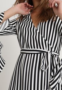 Schwarz-weiß gestreiftes Wickelkleid mit langen Ärmeln und ausgestellten Manschetten sowie einem passenden Gürtel in der Taille. Glatte Stofftextur.