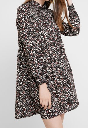 Robe noire à fleurs avec un col smocké haut, des manches longues à élastique et une silhouette fluide, ornée de petites fleurs roses et blanches.