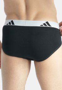 Boxer neri realizzati in tessuto liscio con una cintura elastica bianca caratterizzata da tre strisce nere e un logo sul davanti.