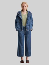 Jeansjacke mit Kapuze, grüner gerippter Oberteil, lässige Jeanshose und schwarze Slipper. Schlichtes Design und entspannte Passform.
