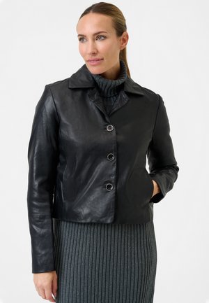 Black leather cropped jacket with a notched collar and three front buttons. Worn over a gray ribbed sweater dress. Smooth texture.