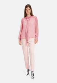 Pinker Bluse mit Punkten, einem Halsband, langen Ballonärmeln und Knopfdetails, kombiniert mit hellpinken Hosen und glänzenden silbernen Ankle Boots.