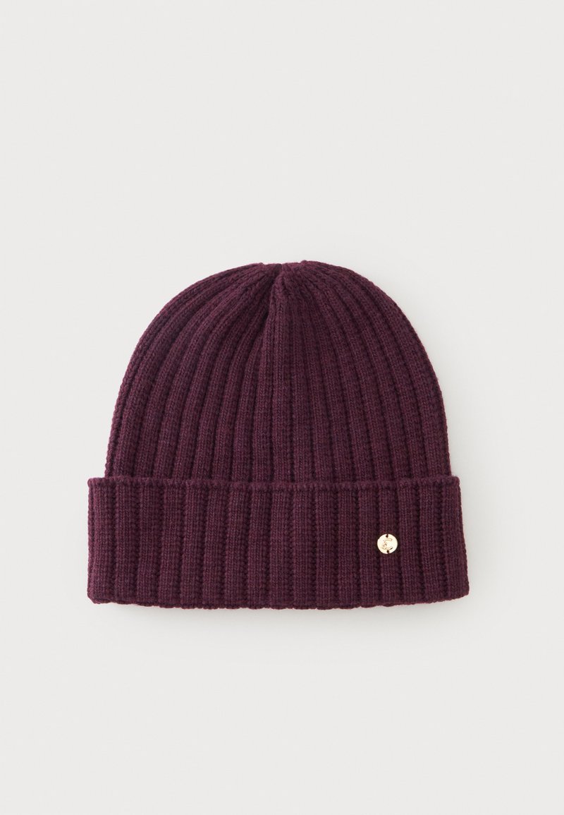 Bonnet en maille côtelée violet foncé avec revers plié et petit emblème rond doré sur le revers sur fond clair.
