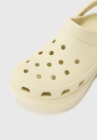Zoccoli giallo chiaro realizzati in materiale flessibile con fori di ventilazione, punta arrotondata e cinturino testurizzato per una vestibilità sicura.