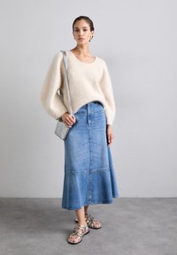 Kremfarget, fluffy strikkegenser, blå denim maxiskjørt, sølv sandaler og en liten rutete crossbody-veske. Teksturert og lagdelt design.