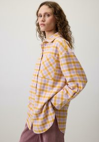 Sárga és levendula kockás ing, gombos elejével, gallérral és egy mellzsebbel, puha, texturált anyagból készült. Hosszú ujjak és ívelt szegély.