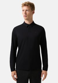 Schwarzes Langarm-Poloshirt aus glattem Stoff. Verfügt über einen Kragen, eine drei Knopfleiste und ein dezentes Logodetail auf der Brust.