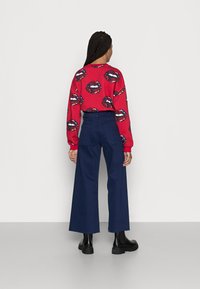 Sweatshirt vermelho com impressões de lábios, combinado com calças largas em tom marinho e botas ankle pretas. O conjunto apresenta um corte descontraído e um material elástico.