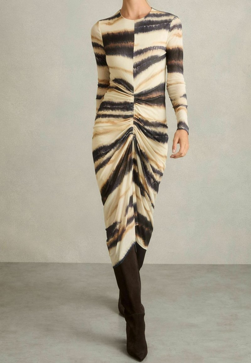 Robe midi à manches longues avec fronces, arborant un motif rayé tigre beige, noir et marron, assortie à des bottes hautes noires jusqu'aux genoux.