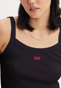 Must mustriba tank top, mille laiade rihmade ja ruudu kujulise kaelusega. Ees on punane Levi's logo silt. Sile tekstuur.