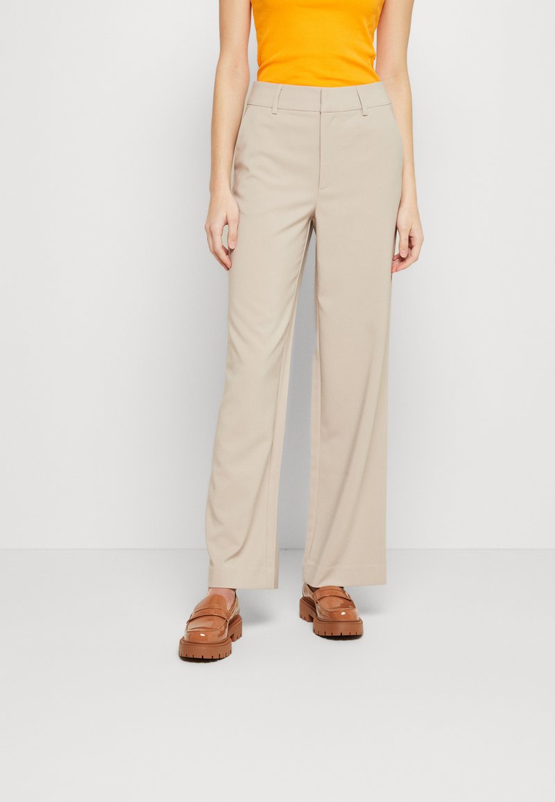 Beige wide-leg trousers with a smooth texture and a high waist, paired with brown loafers. The top is a bright orange sleeveless shirt.
