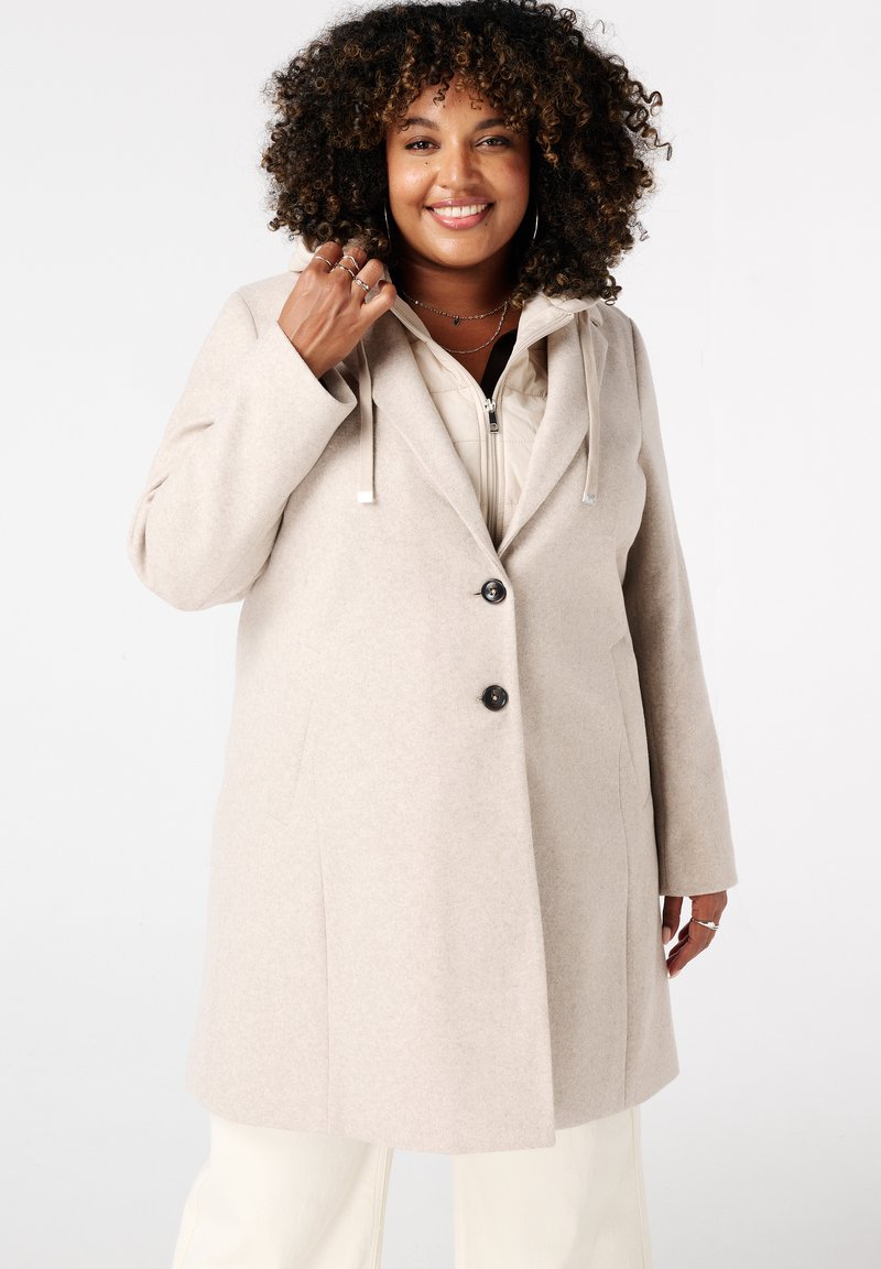 Beige wollen mix coat met een capuchon, voorzien van een sluiting met twee knopen en zijzakken. De binnenkant heeft een lichtgekleurde, gewatteerde voering.