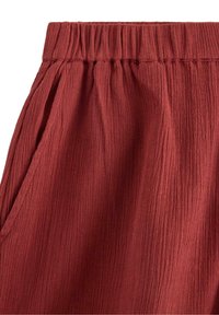 Röd texturerad tyg med ett krusigt mönster och elastisk midja, med sidofickor och lös passform för komfort.