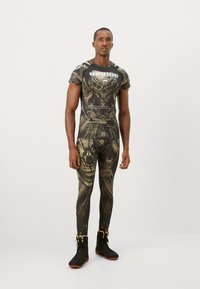 Fitted athletic wear in black and gold with graphic patterns. Short-sleeve top and long leggings, crafted from stretchy material, paired with black sneakers.