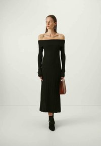 Μαύρο, ριμπ φόρεμα με ώμους έξω, μακριά μανίκια και μήκος μέχρι το πάτωμα. Συνδυασμένο με μια καφέ τσάντα και μαύρες δερμάτινες μπότες μέχρι τον αστράγαλο.