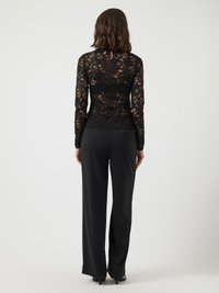 Top in pizzo nero con maniche lunghe e dettaglio a chiave sul retro, abbinato a pantaloni neri a gamba larga, caratterizzati da una texture di tessuto morbida.