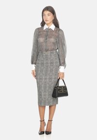 Blusa trasparente a maniche lunghe con colletto bianco, abbinata a una gonna midi aderente con un motivo testurizzato in bianco e nero, e tiene una borsa nera.