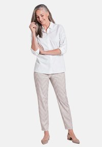 Weißes Hemd mit Kragen, gemusterte hellbeige Hose mit einem subtilen Rautendesign und beige Ballerinas. Glatter Stoff mit hochgerollten Ärmeln.