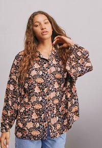 Blusa con estampado floral sobre fondo negro, diseño abotonado y mangas largas. Presenta flores rosas y naranjas en una tela ligera.